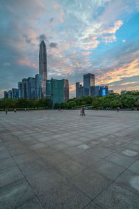 people are riding skateboards around in a park near the city skyline with high rise buildings at twilight