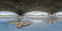 a skateboarder does a trick in front of an overpass that is under a bridge