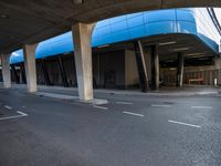 a man skateboarding down a paved road under a highway overpasses with a blue roof