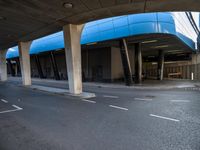 a man skateboarding down a paved road under a highway overpasses with a blue roof