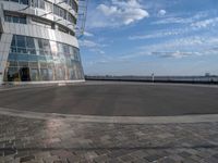 a person doing tricks on a skateboard at an urban park area, next to a walkway and large glass buildings