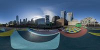 a view from a fish eye lens of buildings in the distance and a painted skateboard park