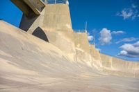 a boy skates through the middle of a large concrete ramp, under a blue sky