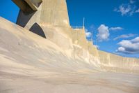 a boy skates through the middle of a large concrete ramp, under a blue sky