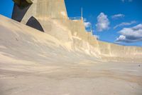 a boy skates through the middle of a large concrete ramp, under a blue sky