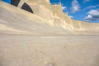 a boy skates through the middle of a large concrete ramp, under a blue sky