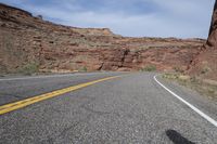 a person riding a motorcycle along a narrow road through rocks and sand cliffs a grassy area on both sides