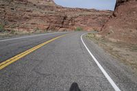 a person riding a motorcycle along a narrow road through rocks and sand cliffs a grassy area on both sides