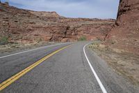 a person riding a motorcycle along a narrow road through rocks and sand cliffs a grassy area on both sides