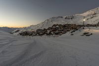 ski lift and buildings with snow covered mountains behind it in the evening sun with the setting light on