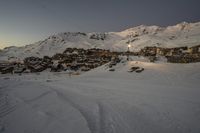 ski lift and buildings with snow covered mountains behind it in the evening sun with the setting light on