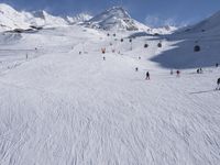 a ski slope full of people with skiers up to the top of it and hills in the background