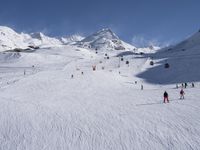 a ski slope full of people with skiers up to the top of it and hills in the background