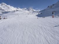 a ski slope full of people with skiers up to the top of it and hills in the background