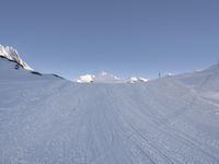 a person snow skiing down a ski slope in the mountains under a blue sky with some clouds