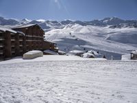 a snow covered ski slope next to a lodge with many windows in a mountainous area