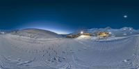 a ski slope with several tracks and buildings in the distance at night time, seen from the bottom