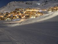 a ski slope going up a snow covered hillside with houses lit up at night in the background