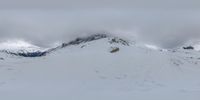 skiers are riding down the side of a mountain in the snow on a cloudy day