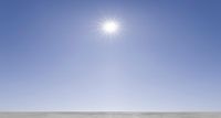 a person skis across a vast frozen surface, surrounded by the sun on a sunny day