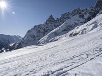 a person is skiing on the snow with mountain tops and sun shining in the sky