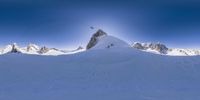 a skier is descending a steep snowy hill towards the mountain peaks and mountains, with a snowboarder on top