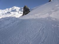 a person skis along the side of a steep snowy hill in the mountains, with a rock out to the right of it