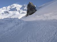 a person skis along the side of a steep snowy hill in the mountains, with a rock out to the right of it