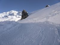 a person skis along the side of a steep snowy hill in the mountains, with a rock out to the right of it