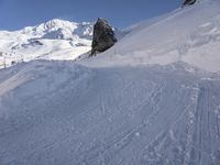 a person skis along the side of a steep snowy hill in the mountains, with a rock out to the right of it