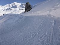 a person skis along the side of a steep snowy hill in the mountains, with a rock out to the right of it