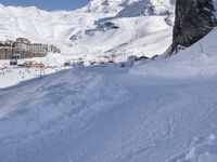 a man riding skis down a snow covered slope next to tall buildings on a mountain