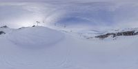 snow boarder rides the side of a mountain with sky in background while snow skiier is seen from a distance