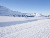 a person skiing on the snowy ground in front of snow capped mountains and blue skies