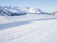 a person skiing on the snowy ground in front of snow capped mountains and blue skies