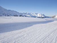 a person skiing on the snowy ground in front of snow capped mountains and blue skies