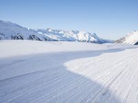 a person skiing on the snowy ground in front of snow capped mountains and blue skies