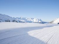 a person skiing on the snowy ground in front of snow capped mountains and blue skies