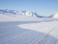 a person skiing on the snowy ground in front of snow capped mountains and blue skies