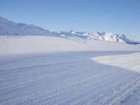 a person skiing on the snowy ground in front of snow capped mountains and blue skies