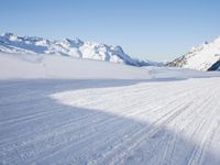 a person skiing on the snowy ground in front of snow capped mountains and blue skies