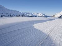 a person skiing on the snowy ground in front of snow capped mountains and blue skies