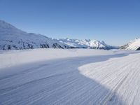 a person skiing on the snowy ground in front of snow capped mountains and blue skies