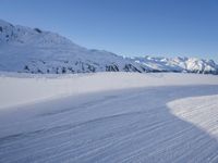 a person skiing on the snowy ground in front of snow capped mountains and blue skies