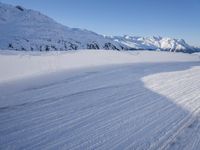 a person skiing on the snowy ground in front of snow capped mountains and blue skies