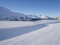 a person skiing on the snowy ground in front of snow capped mountains and blue skies