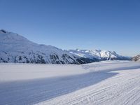 a person skiing on the snowy ground in front of snow capped mountains and blue skies