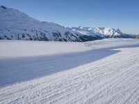 a person skiing on the snowy ground in front of snow capped mountains and blue skies