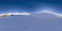 snow covered mountains in the distance with many tracks of skiers on the ground and cars parked below