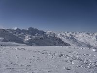 a lone skier on a snowy hill looking over the valley and snow - covered peaks